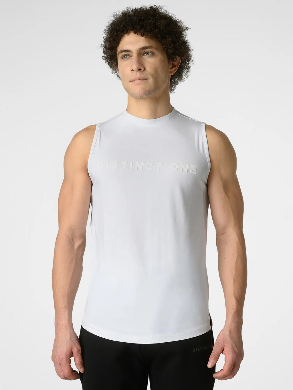 A man wearing a white sleeveless athletic tank top with 'DISTINCT ONE' printed across the chest in a subtle tonal font, paired with black athletic pants, against a light gray studio background.